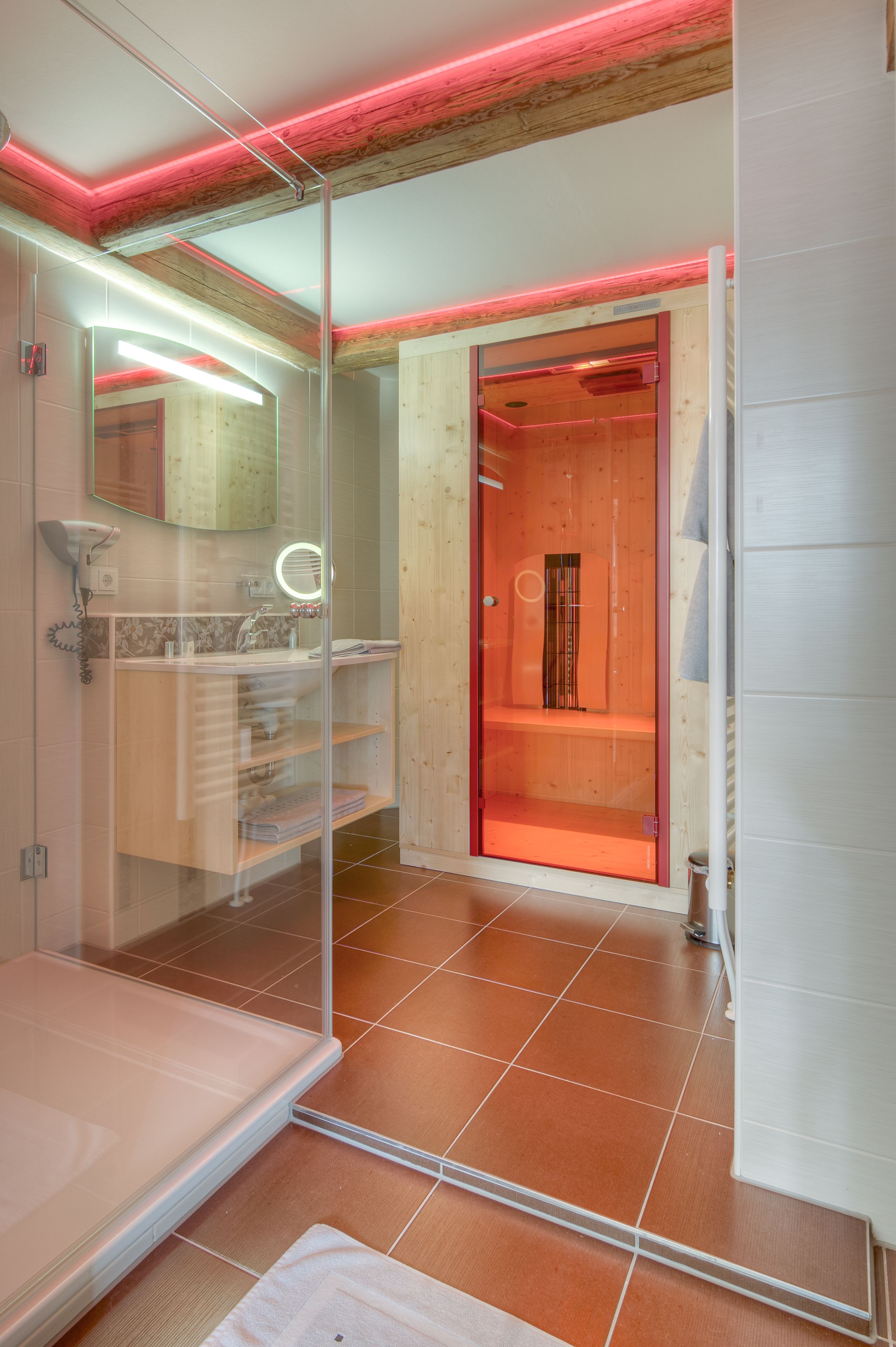 A modern bathroom with a glass shower enclosure, a wooden vanity, and a red-framed door leading to a shower area.
