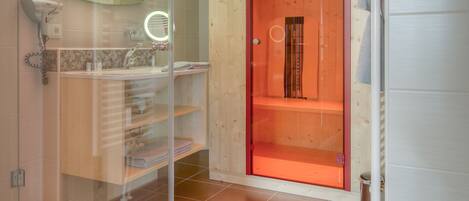 A modern bathroom with a glass shower enclosure, a wooden vanity, and a red-framed door leading to a shower area.