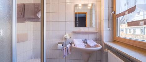 A bathroom with a shower, a sink, and a window.