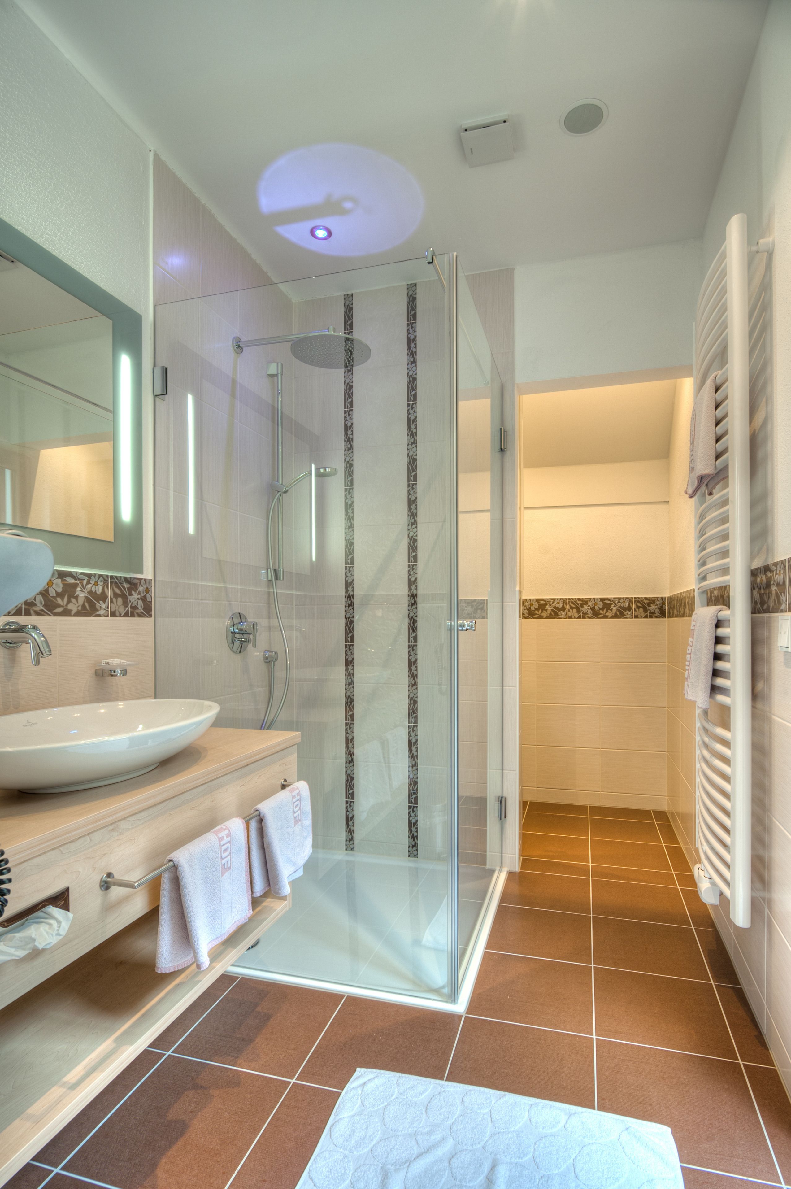 Een moderne badkamer met een douche met glazen wand, een wastafel met spiegel en een handdoekrek.
