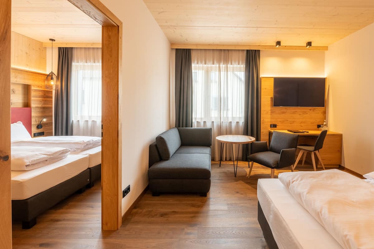 A hotel room with a bed, a sofa, a desk with chairs, and a TV.