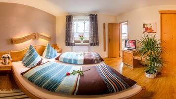 A cozy bedroom with a large bed, bedside tables, a TV, and a potted plant.