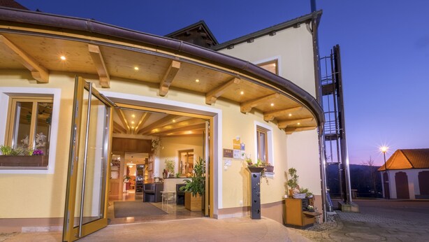 A hotel entrance with a curved wooden overhang, a reception desk, and a staircase leading to the upper floors. - Landhotel Goldenes Kreuz (Moosbach)
