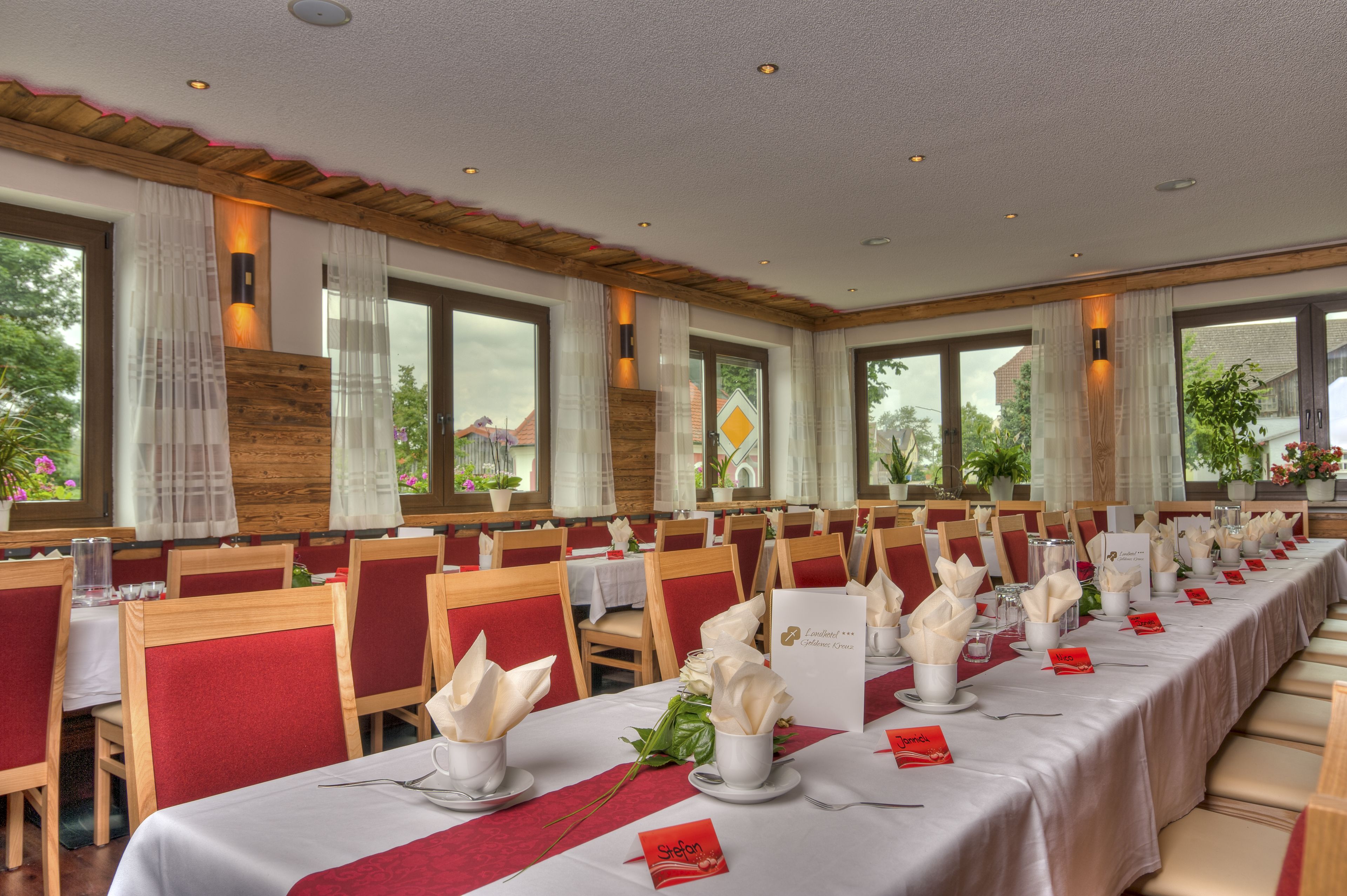 A long dining table set with white tablecloths, red chairs, and floral centerpieces.