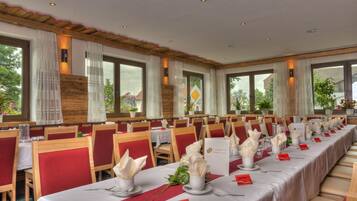Una larga mesa de comedor dispuesta con manteles blancos, sillas rojas y centros de mesa florales.