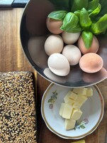 A bowl of eggs, a plate of cheese, and a tray of sesame seeds on a wooden table.