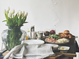 Desayuno con un jarrón de tulipanes, una bandeja de cruasanes, queso y diversas opciones para untar.
