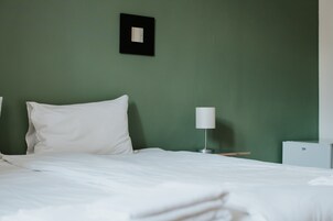 Una cama bien hecha con sábanas blancas en una habitación con paredes verdes.