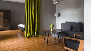 A modern living room with a wooden floor, a grey sofa, a round table with a vase of flowers, and a green curtain. - Bookinn B&B (Vilnius)