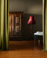 Una habitación con un armario de madera, una lámpara roja y una cama con ropa blanca.