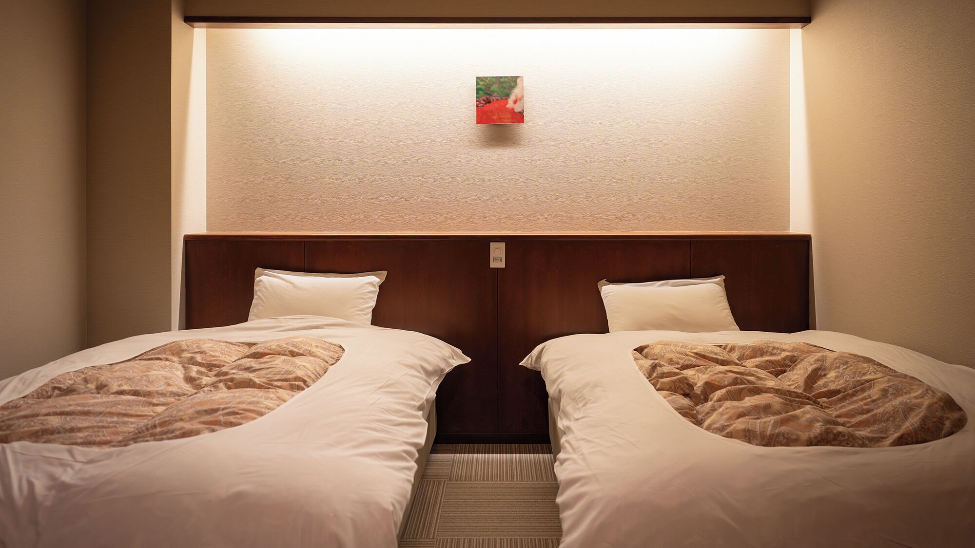 Una habitación de hotel con dos camas, un cabecero y un pequeño cuadro en la pared.