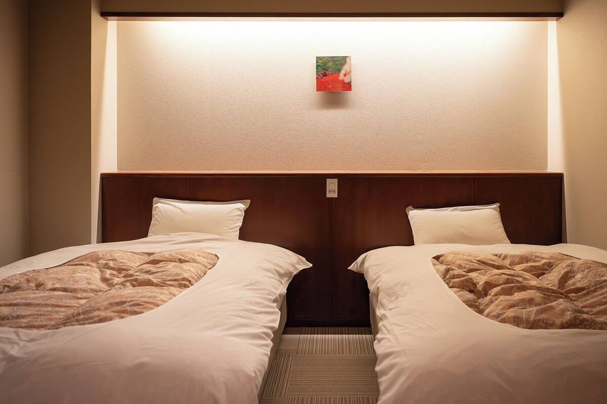Una habitación de hotel con dos camas, un cabecero y un pequeño cuadro en la pared.