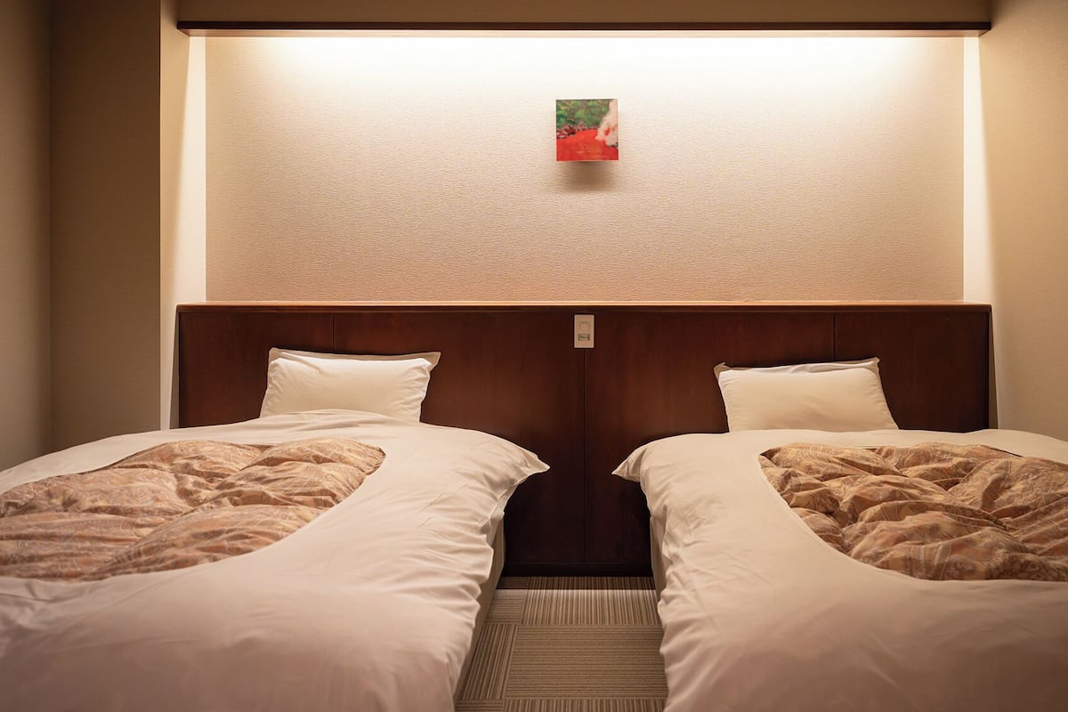 Una habitación de hotel con dos camas, un cabecero y un pequeño cuadro en la pared.