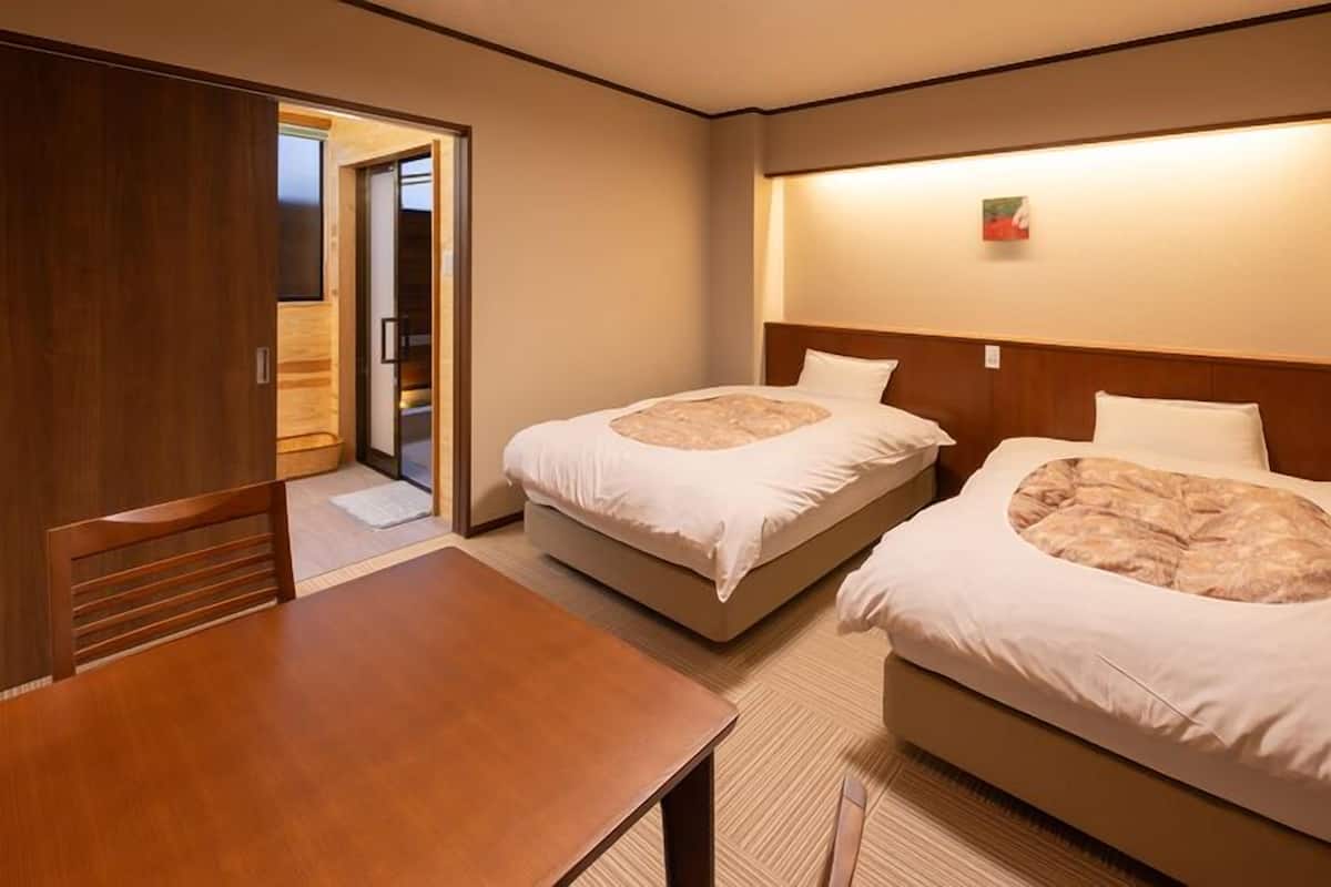 Una habitación de hotel con dos camas, una mesa de madera y un armario.