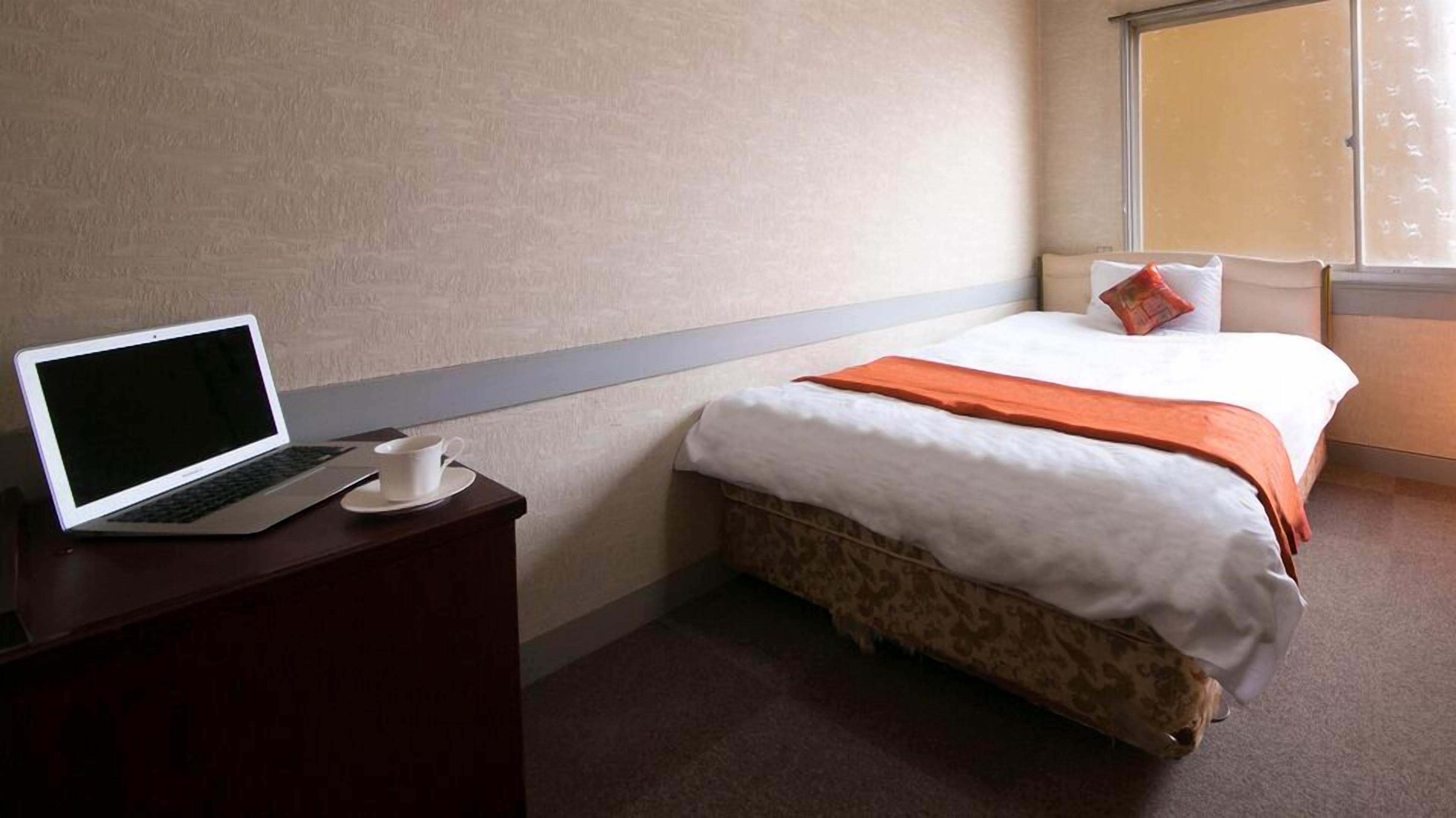 Een hotelkamer met een bed, een bureau met een laptop en een kopje.