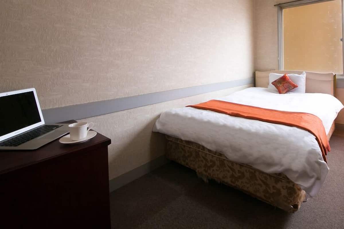 Een hotelkamer met een bed, een bureau met een laptop en een kopje.