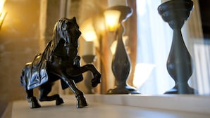 A black horse figurine on a white surface, with a candle and a vase in the background.
