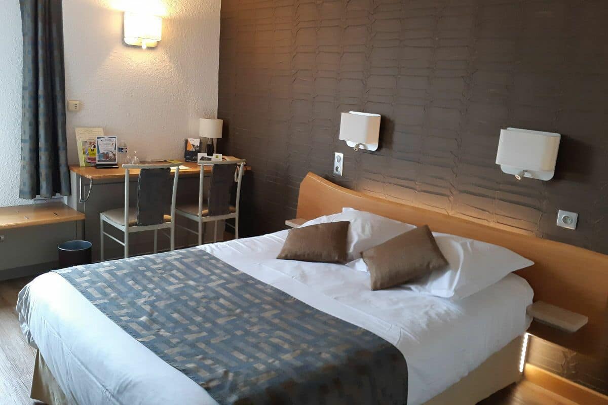 Une chambre d’hôtel comprenant un lit, des tables de chevet, un bureau avec une chaise et des lampes fixées au mur.