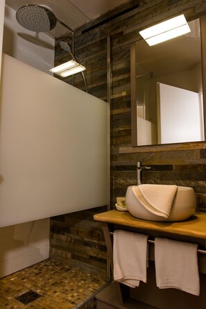 A modern bathroom with a stone wall, a large mirror, a round sink, and a showerhead. - Hôtel restaurant Le Cheval Rouge (Sainte-Menehould)