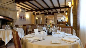 Restaurante com mesas redondas preparadas para refeições, com toalhas brancas, copos de vinho e talheres.