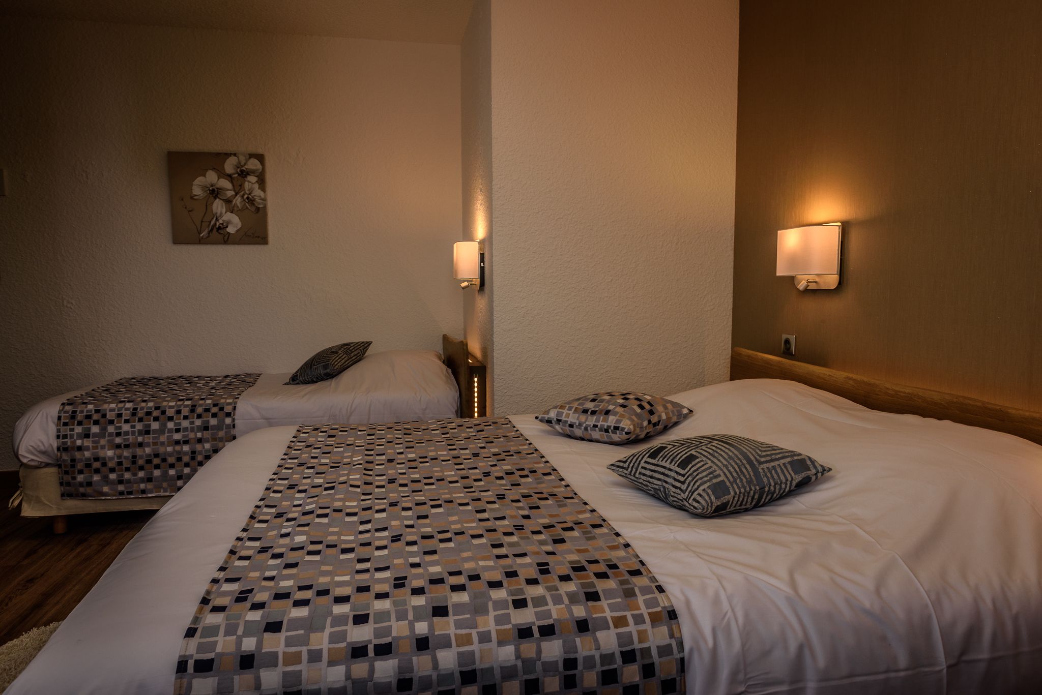 Een hotelkamer met twee bedden, elk voorzien van beddengoed en kussens met een patroon. Er hangen wandlampen en een schilderij aan de muur.