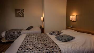 Een hotelkamer met twee bedden, elk voorzien van beddengoed en kussens met een patroon. Er hangen wandlampen en een schilderij aan de muur.