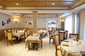 A restaurant with multiple tables set for dining, wooden chairs, and a central column. - Hôtel restaurant Le Cheval Rouge (Sainte-Menehould)