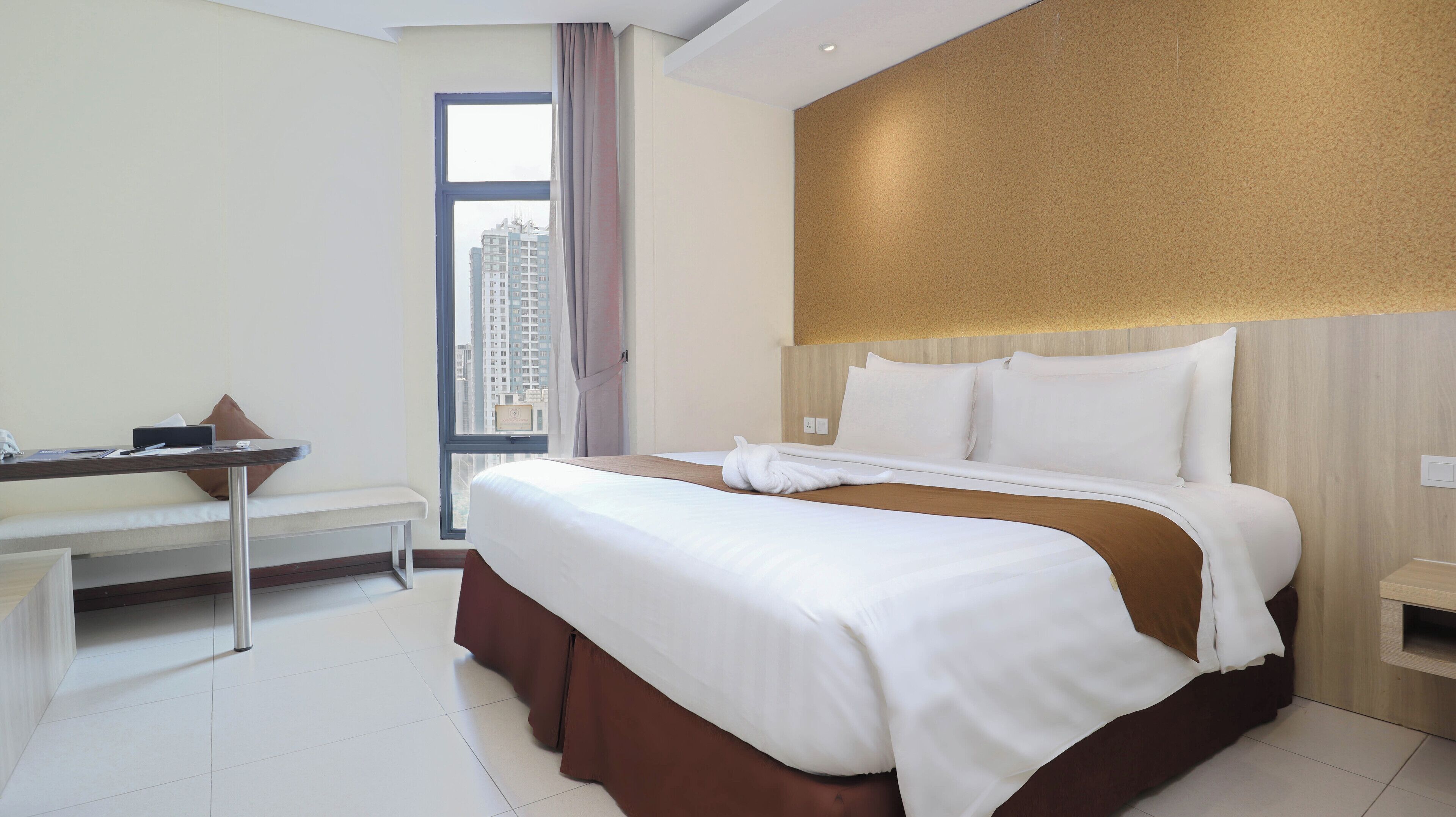 A hotel room with a bed, a desk, and a view of tall buildings.