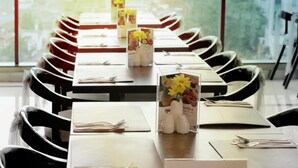 A conference room with a long table, black chairs, and a menu stand with yellow flowers. - Vasaka Hotel Jakarta managed by DAFAM (Jakarta)