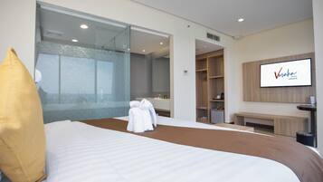 A hotel room with a large bed, a glass wall, a TV, and a wardrobe.