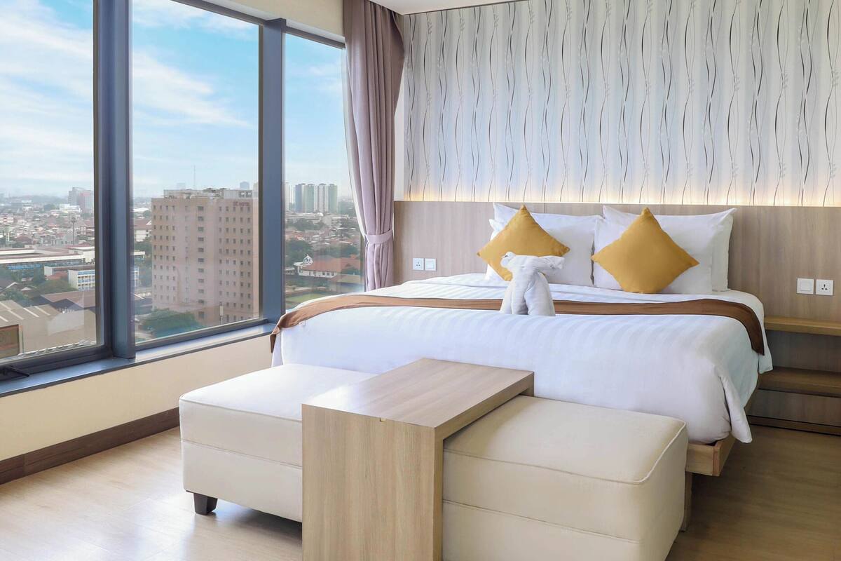 A modern hotel room with a large bed, a bedside table, and a view of the city.