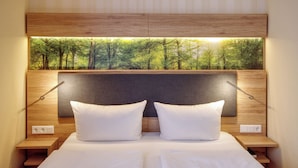 Un lit bien fait, avec du linge de lit blanc et des oreillers, une tête de lit en bois donnant sur une forêt, et des lampes de chevet.