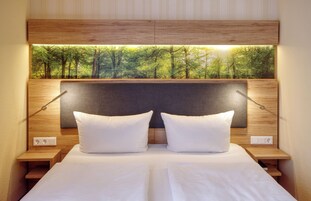 A neatly made bed with white linens and pillows, a wooden headboard with a forest view, and bedside lamps.