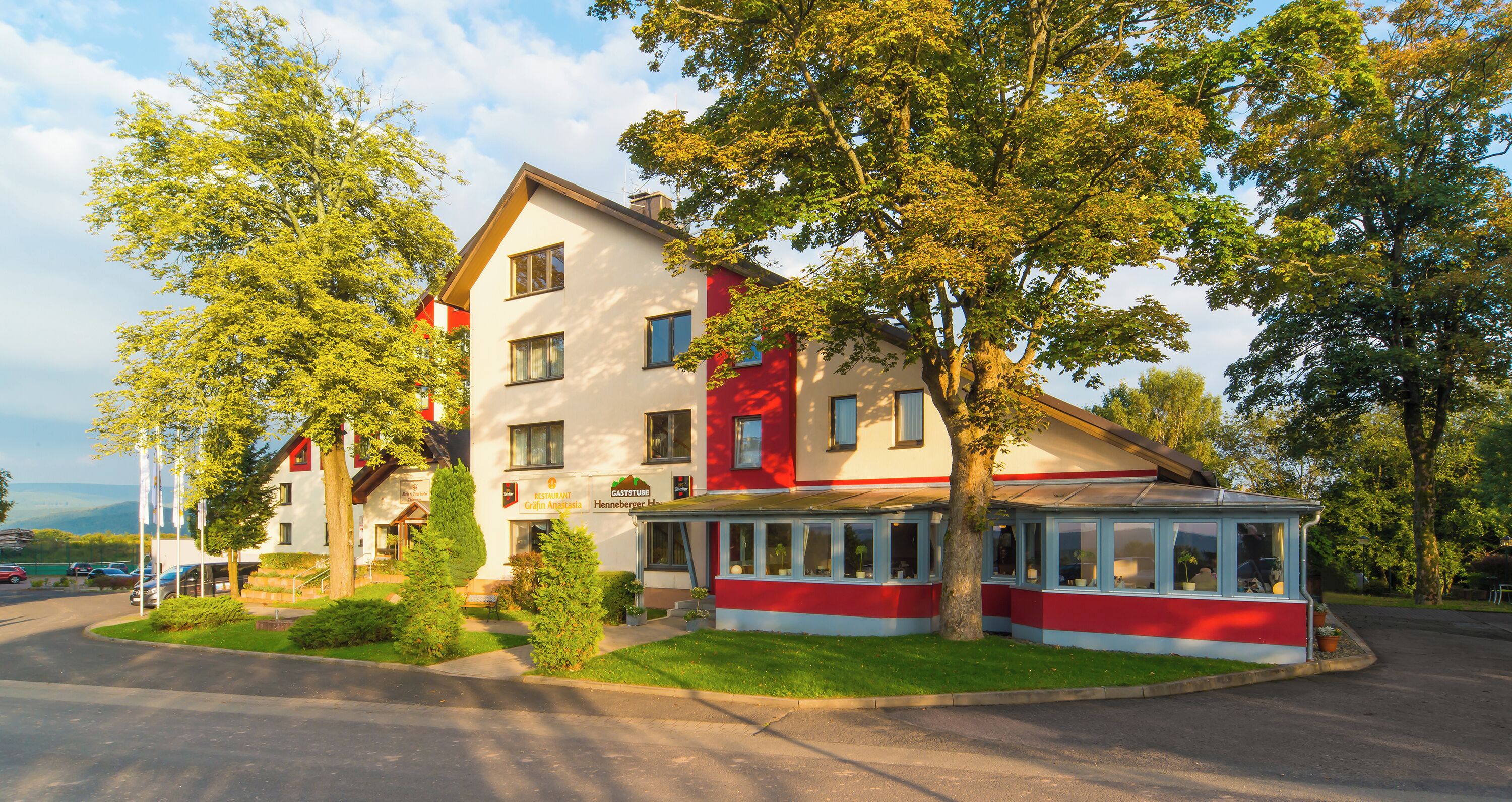 Ett hotell med flera våningar, en restaurang på bottenvåningen och omgivet av träd och en parkeringsplats.