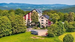 Un hôtel à plusieurs étages, doté d’une façade rouge et blanche, entouré d’une végétation luxuriante et comprenant un espace de stationnement.
