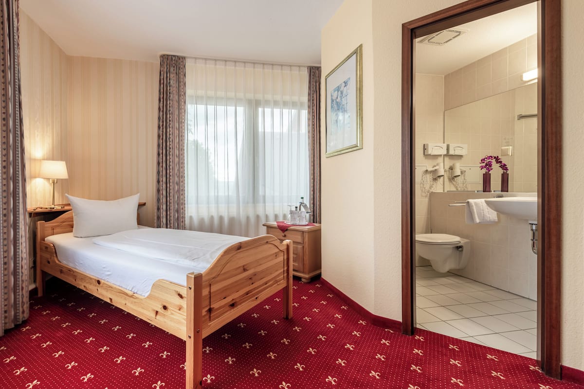 Une chambre d’hôtel avec un lit en bois, une table de chevet avec une lampe, un miroir et une vue sur la salle de bain.