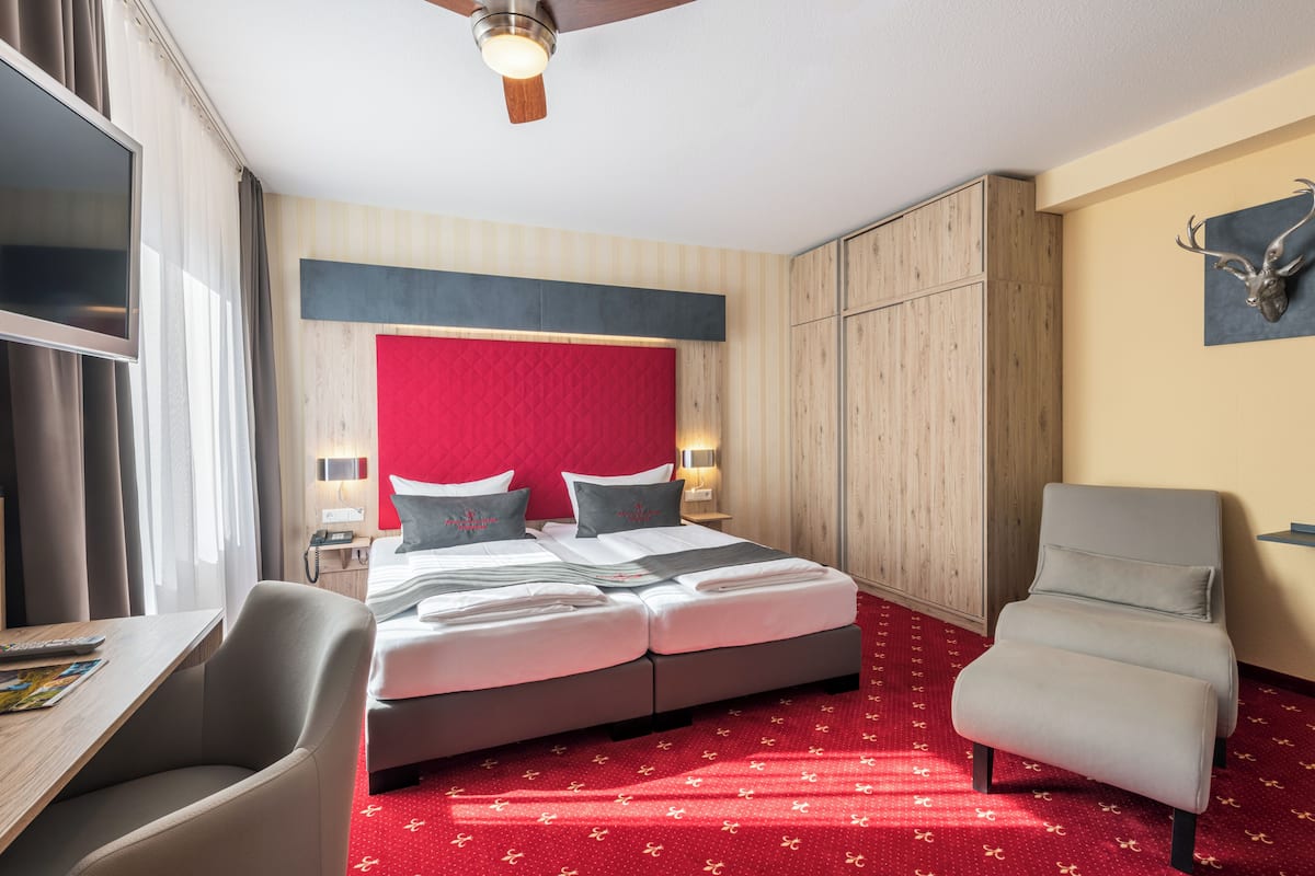 Une chambre d’hôtel équipée d’un lit, d’un bureau, d’une chaise, d’un ventilateur de plafond et d’une tête de cerf fixée au mur.