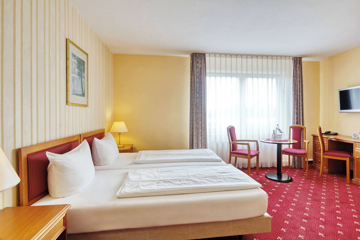 Une chambre d’hôtel avec deux lits, un bureau, une chaise, une télévision et une fenêtre avec des rideaux.