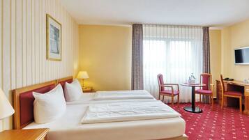 A hotel room with two beds, a desk, a chair, a TV, and a window with curtains.
