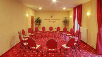 Ein Konferenzraum mit roten, kreisförmig angeordneten Stühlen, einem Teppichboden und einer Wand mit dem Namen des Hotels.