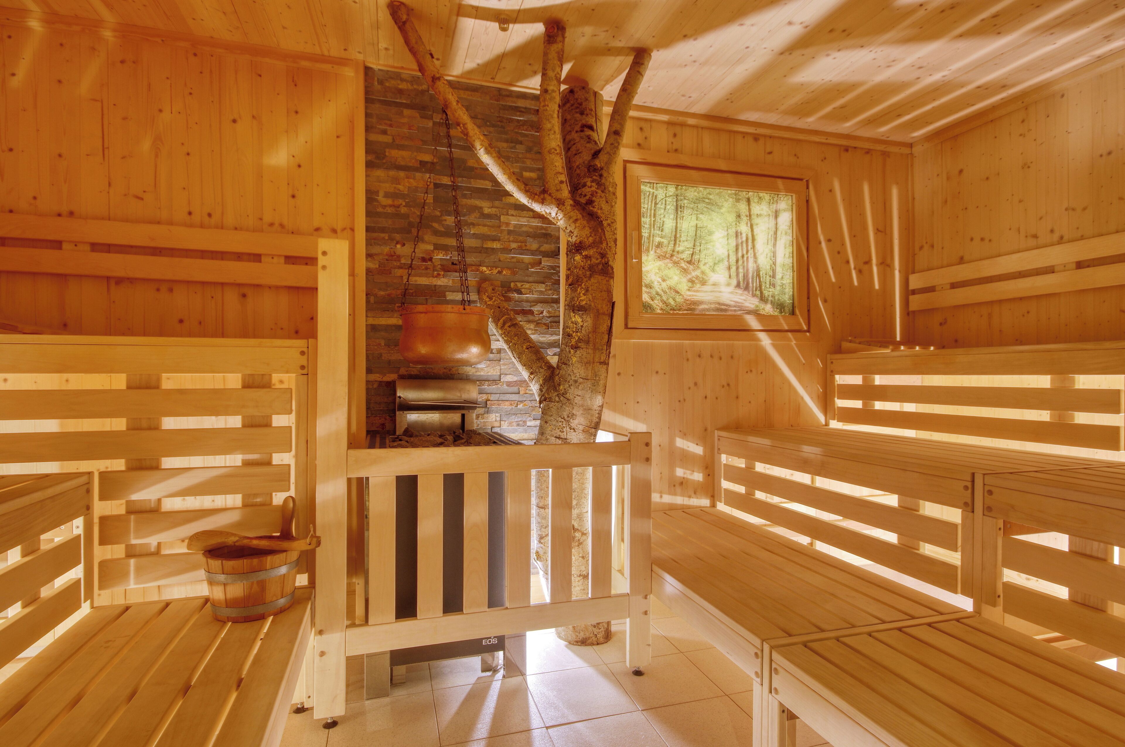 Una sauna de madera con bancos, una pared de piedra y un ventanal con vistas al bosque.