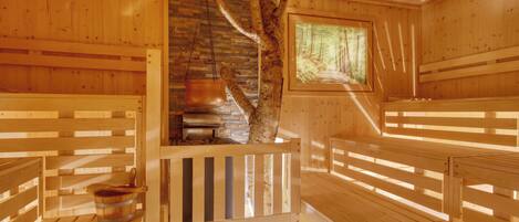 A wooden sauna with benches, a stone wall, and a window with a forest view.