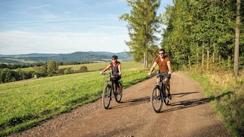 Two cyclists on a dirt path surrounded by greenery and hills.