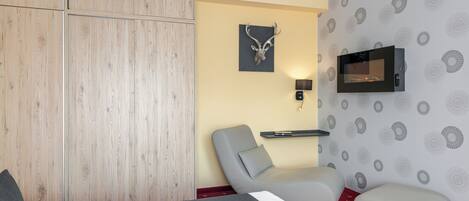 Une chambre d’hôtel avec un lit, un fauteuil gris, une petite table, un téléviseur fixé au mur et un élément décoratif mural.