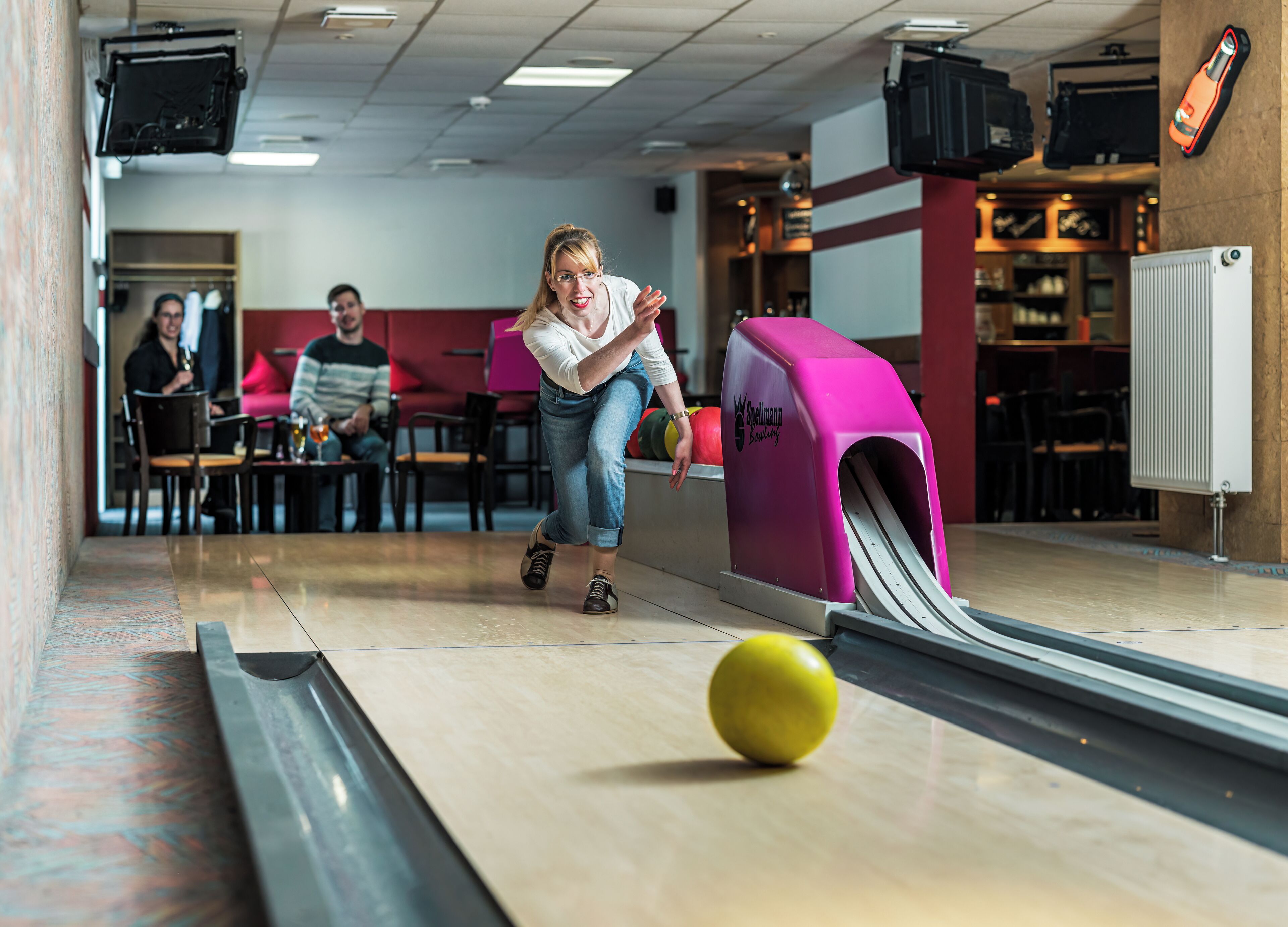 Une salle de bowling avec une piste rose, une boule de bowling et une personne qui joue au bowling.