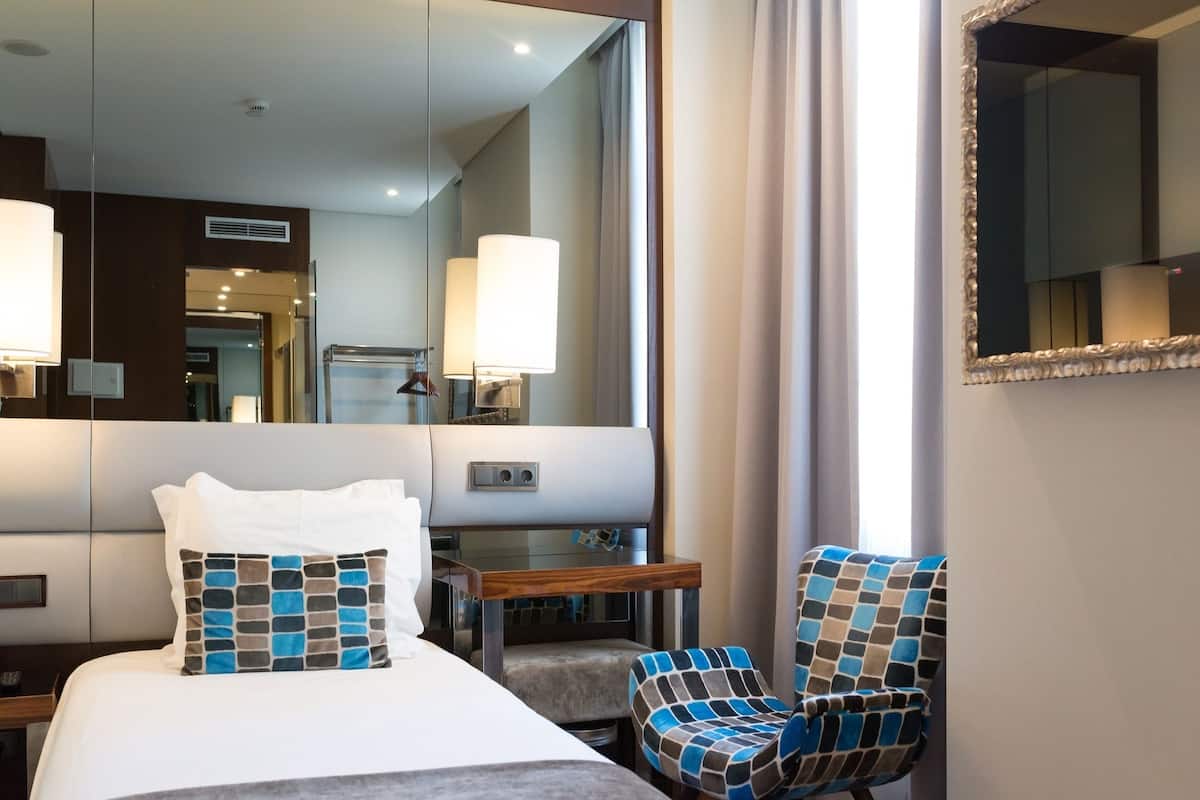 Habitación de hotel con una cama, una silla, un escritorio y un espejo grande.