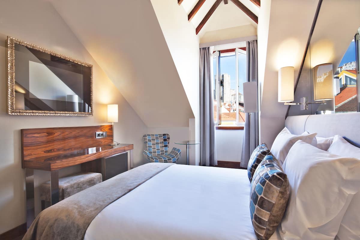 Una habitación de hotel con una cama grande, un escritorio de madera, una silla y un espejo.
