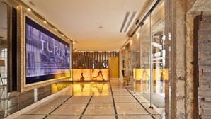 Un hall d’hôtel doté d’un grand écran numérique d’accueil, d’un sol carrelé et d’un mur en verre avec une façade en briques.