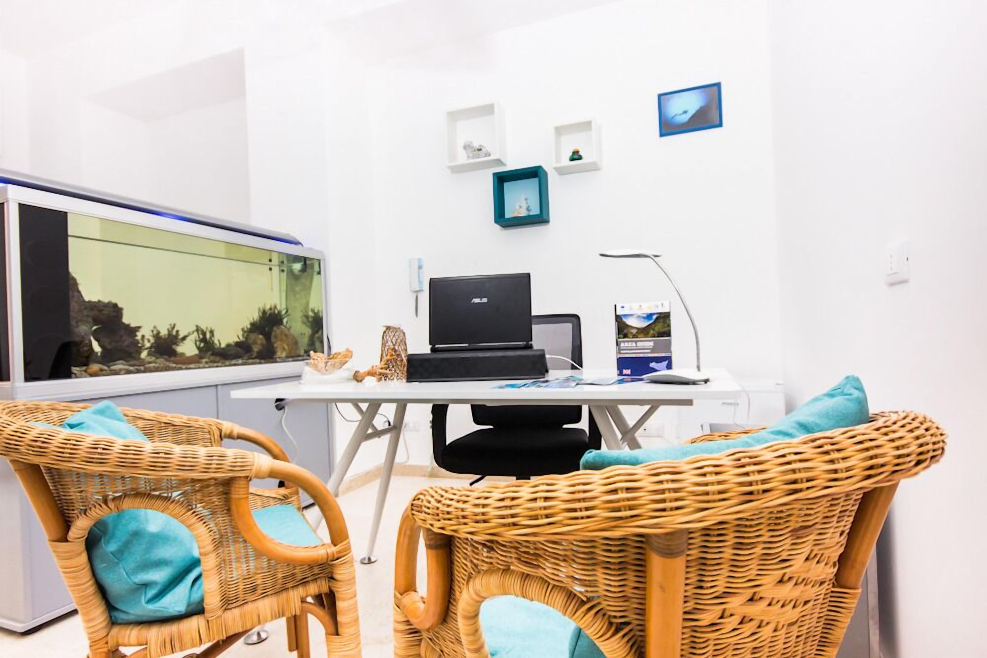 A room with a desk, computer, and a fish tank. There are wicker chairs with cushions.