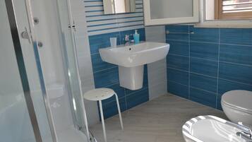 A bathroom with a shower, sink, toilet, and a small stool.